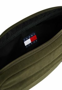Pochette zippée vert olive avec doublure intérieure noire et une étiquette logo Tommy Jeans cousue à l'intérieur.