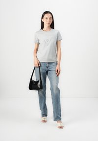 Grå t-skjorte med korte ermer og logo, kombinert med lysvaskede denimjeans, svart håndveske og beige slip-on sandaler med merkevarelogo.