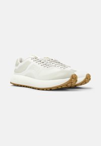 Sneaker bianche alla moda con accenti grigio chiaro, caratterizzate da una suola testurizzata e stringhe, su uno sfondo bianco semplice.