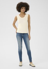 Krämfärgad ribbad linne med rundad halsringning, kombinerad med slim fit blå jeans och ljusa loafers. Avslappnad outfit.