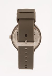 Correa de reloj de silicona gris con hebilla de metal, que muestra una esfera de reloj circular con componentes internos visibles y un diseño minimalista.