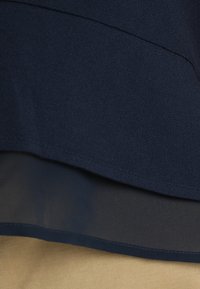 Tissu en couches bleu foncé avec une couche inférieure transparente et une surface beige en dessous, montrant un contraste entre textile texturé et lisse.