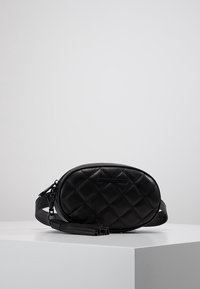 Bolso negro de cuero acolchado con forma ovalada, presenta una correa desmontable y un acento frontal plano. Su textura es suave con patrones de diamantes en relieve.