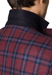 Kurtka w kratę z czerwono-czarnym wzorem, wykonana z teksturowanej tkaniny z kołnierzem przypominającym wełnę w kolorze czarnym. Widoczne detale szycia.