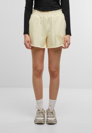 Cream-colored shorts with an elastic waistband, side pockets, and a decorative embroidered butterfly detail on the right hem.