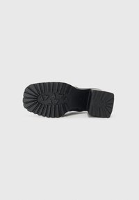 Semelle de botte en caoutchouc noir présentant un motif de crampons robuste avec de profondes rainures pour l'adhérence, et un talon rectangulaire au fini lisse.