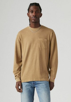 Tan langærmet skjorte med en lomme, lavet af tekstureret bomuldsstof og diskret Levi's branding. Sammen med lyseblå jeans.