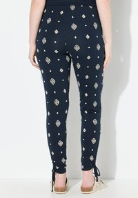 Granatowe legginsy wykonane z elastycznego materiału z kremowymi wzorami geometrycznymi. Posiadają marszczenia na kostkach i wiązania. Gładka tekstura i dopasowany krój.