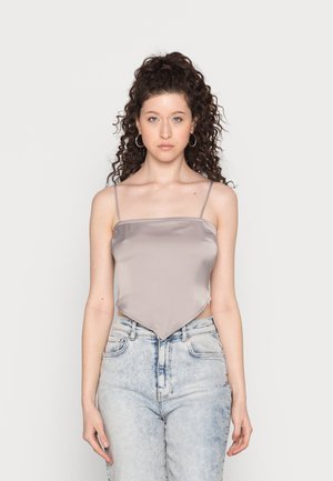 Top curto de seda cinza com alças finas e bainha pontuda, combinado com jeans de cintura alta azul claro, apresentando texturas esmaecidas.