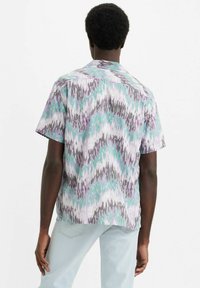 Camisa de manga corta en tejido ligero con un patrón de zigzag multicolor en morado, verde y gris. Corte relajado con un yugo en la parte posterior.