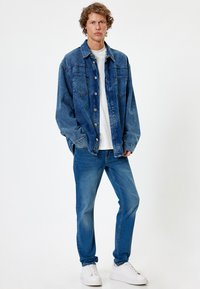 Chaqueta de mezclilla con un corte relajado, color azul, dos bolsillos en el pecho, cierre de botones, combinada con jeans de un tono azul claro y zapatillas blancas.