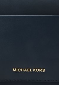Mørkeblå struktureret tekstil med en glat læderdetalje. Guld "MICHAEL KORS" logo præsenteret fremtrædende. Minimalistisk design, ingen mønstre.