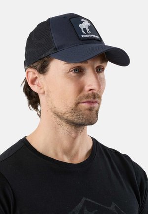 Man met lichte baard die een zwarte pet draagt met een wit elandlogo en het woord "SwedenMount", en een zwart shirt met ronde hals.