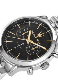 Chronografur med sort urskive, sølvfarvet kasse, guld accenter, tre under-urskiver og et armbånd af rustfrit stål. Rund form, poleret finish.