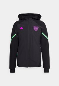 Veste de sport noire à capuche avec des bandes vertes sur les manches, logo Adidas violet et écusson du FC Bayern Munich sur la poitrine, fermeture éclair devant.