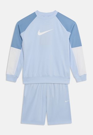 Vaaleansininen Nike-urheiluasu, jossa on valkoiset ja tummansiniset koristehihat, pitkähihainen paita logolla ja sitä vastaavat shortsit.