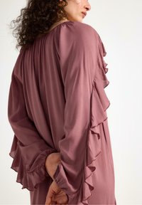 Långärmad klänning i mjuk mauve-nyans, med volangdetaljer längs ärmarna och en avslappnad passform med en rynkad halslinning.