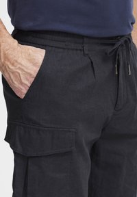 Svart cargo-bukser laget av lett stoff, med elastisk midje, snor og sidelommer med klaffdetalj.