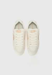Cream-colored sneakers with a textured upper, featuring light pink accents and tonal stitching, round toe, and white laces.