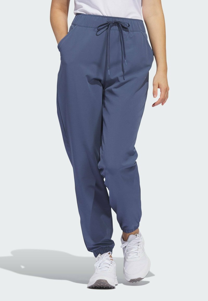 Pantalons de jogger bleu marine avec une taille élastique, cordon de serrage et poches latérales ; chevilles resserrées. Portés avec des baskets blanches.