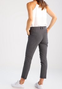 Pantaloni grigi su misura con vestibilità slim, texture sottile e tasche laterali, abbinati a sneakers bianche e un top senza maniche.