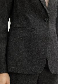 Dark gray textured blazer with a single black button, front flap pockets, and matching trousers worn on a person.