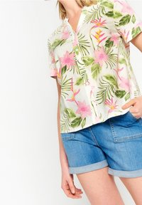 Short-sleeved floral shirt in light fabric, featuring pink flowers and green leaves, button front, paired with denim shorts.