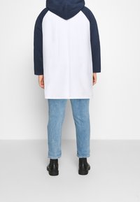 Felpa con cappuccio bianca con maniche raglan blu navy, caratterizzata da una vestibilità ampia, che arriva fino a metà coscia, abbinata a jeans blu chiaro e stivali neri.
