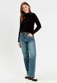 Sort langærmet sweater med høj hals; lyseblå lige ben jeans; sort bælte; solide sort-hvide sko.