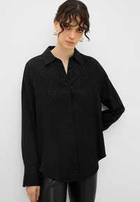 Camicia nera con stampa leopardata, con bottoni frontali, colletto e maniche lunghe, realizzata in un tessuto liscio con una leggera lucentezza.