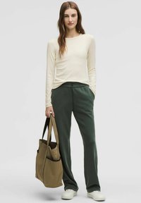 Langärmliges cremefarbenes Oberteil kombiniert mit grünen Sweatpants und einer braunen Tragetasche. Das Outfit zeichnet sich durch eine lockere Passform und weiche Texturen aus.