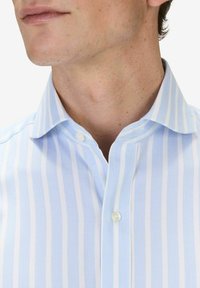 Vaaleansininen ja valkoinen raidoitettu paitapusero, jossa on napitettava kaulus, ja joka on valmistettu sileästä kankaasta, jossa on hienostunut kiilto.