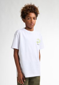Tricou alb din bumbac, cu un design grafic verde și negru pe pieptul stâng, cu mâneci scurte și o croială lejeră.