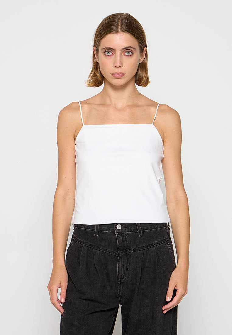 Weißes Satin-Camisole mit dünnen Trägern, quadratischem Ausschnitt und glatter Textur; kombiniert mit lockeren schwarzen Hosen für den Kontrast.