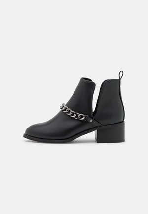Schwarzer Knöchelstiefel mit niedrigem Blockabsatz, offenem Seitenausschnitt, Zuglasche hinten und dekorativer silberner Kette vorne.