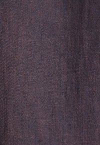 Textielstof in donkerpaars en bordeauxrode tinten met een gestructureerd, geweven patroon. Het oppervlak vertoont lichte kleur- en weefvariaties.