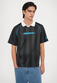 Melna un pelēka svītraina polo krekla ar baltu apkakli, ar zilu Reebok logo un šuvēm. Izgatavots no gludas, sportiskas auduma.