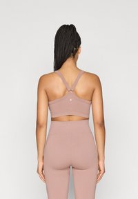 Αθλητικό σουτιέν σε φωτεινό μωβ με ριμπ υφή, τιράντες που διασταυρώνονται στην πλάτη και κυκλικό διακοσμητικό στοιχείο. Συνδυασμένο με αντιστοιχία ψηλόμεσο κολάν.