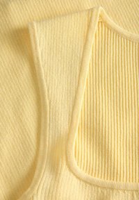 Κοντινό πλάνο απαλού κίτρινου πλεκτού υφάσματος με ριγέ υφή που δείχνει την υφή και τις καμπυλωτές άκρες ενός ρούχου χωρίς μανίκια.