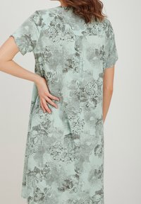 Kukkamekko vaaleanvihreänä, jossa on lyhyet hihat ja mustavalkoinen teksturoitu kuvio. Selässä on tyylikäs tuuletusaukko.