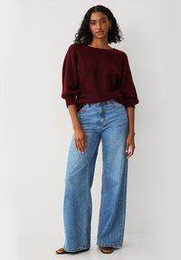 Pull bordeaux surdimensionné avec des manches amples, associé à un jean large bleu clair. Des chaussures imprimé animal et des bagues complètent la tenue.