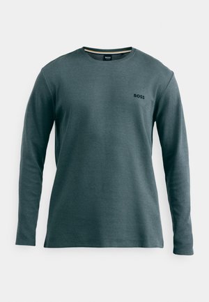 T-shirt à manches longues en vert sarcelle avec un tissu texturé. Présente un petit logo noir sur la poitrine gauche et une rayure contrastante au col.