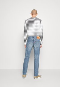 Camisa de manga larga a rayas en blanco y negro, combinada con jeans azul claro con parche de logo; zapatillas casuales completan el conjunto.