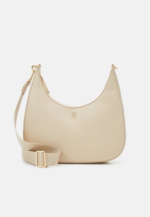 Beige leren schoudertas met een gebogen silhouet, gouden hardware accenten, verstelbare strap en een subtiele logo detail aan de voorkant.