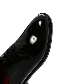 Glanzend zwart leren nette schoen met gesloten veters en ronde neus, gefotografeerd tegen een witte achtergrond.