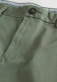 Pantalones cortos de algodón verde con un frente plano, que cuentan con un cierre de botón negro. Ligera textura con detalles de raya horizontal en el interior de la cinturilla.