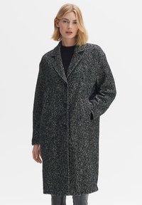 Houndstooth coat in black and white with a notch collar, single-button closure, two side pockets, and a relaxed fit. Soft woven texture.