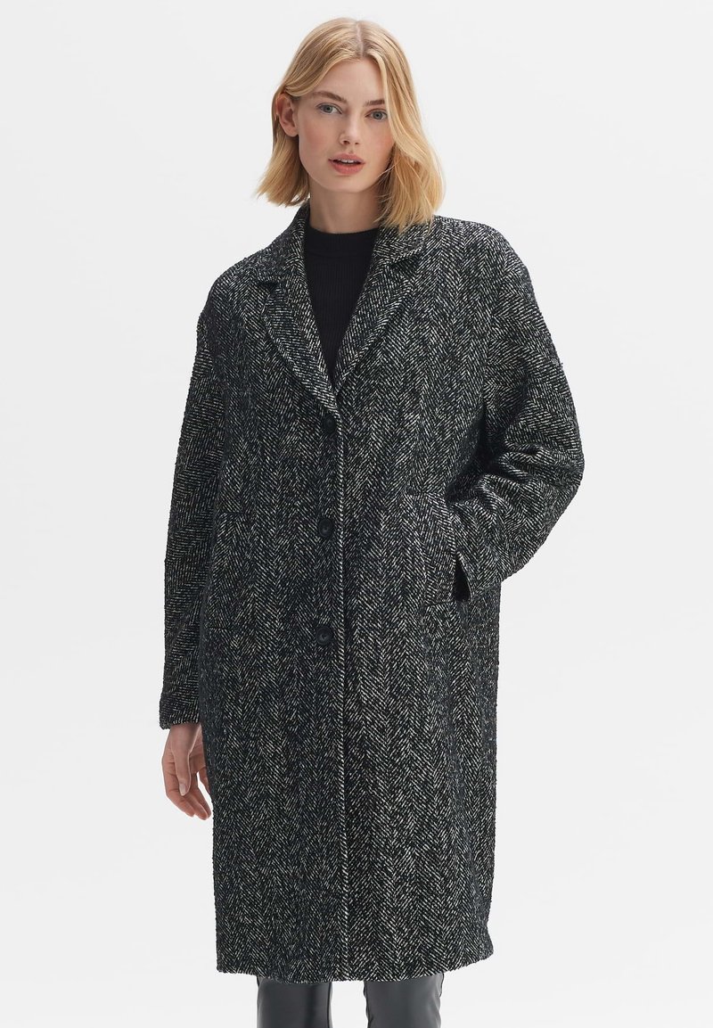 Houndstooth coat in black and white with a notch collar, single-button closure, two side pockets, and a relaxed fit. Soft woven texture.