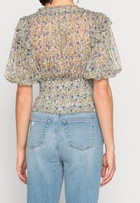 Blus med blommönster, halvgenomskinlig, med puffärmar, rynkad byst och smockad midja, tillsammans med ljusblå denimjeans.