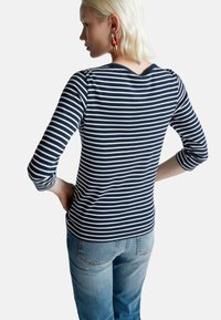 Navy i biały w pasiasty shirt z rękawami do trzech czwartych, okrągłym dekoltem i dopasowanym krojem, w połączeniu z jasnoniebieskimi dżinsami.